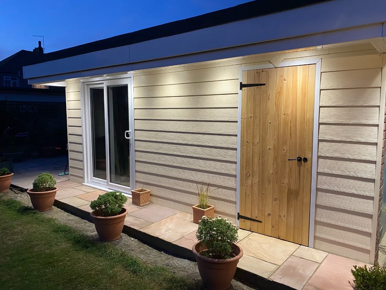 Garden room clad in pale embossed horizontal Fortex-style cladding with a timber door