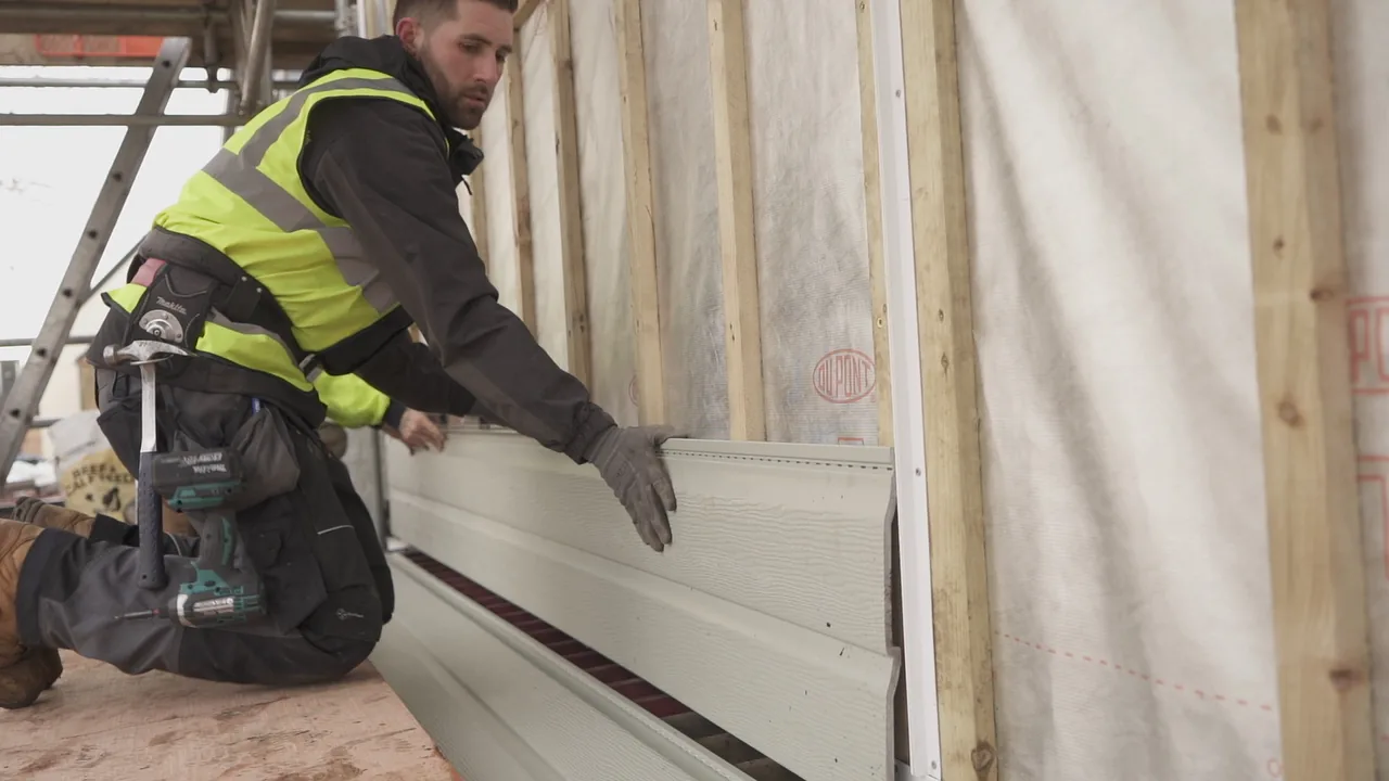 Installer fixing pale embossed Fortex weatherboard cladding to an exterior wall