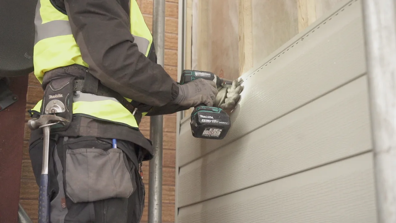 Tradesperson positioning embossed cladding boards during installation on an external wall